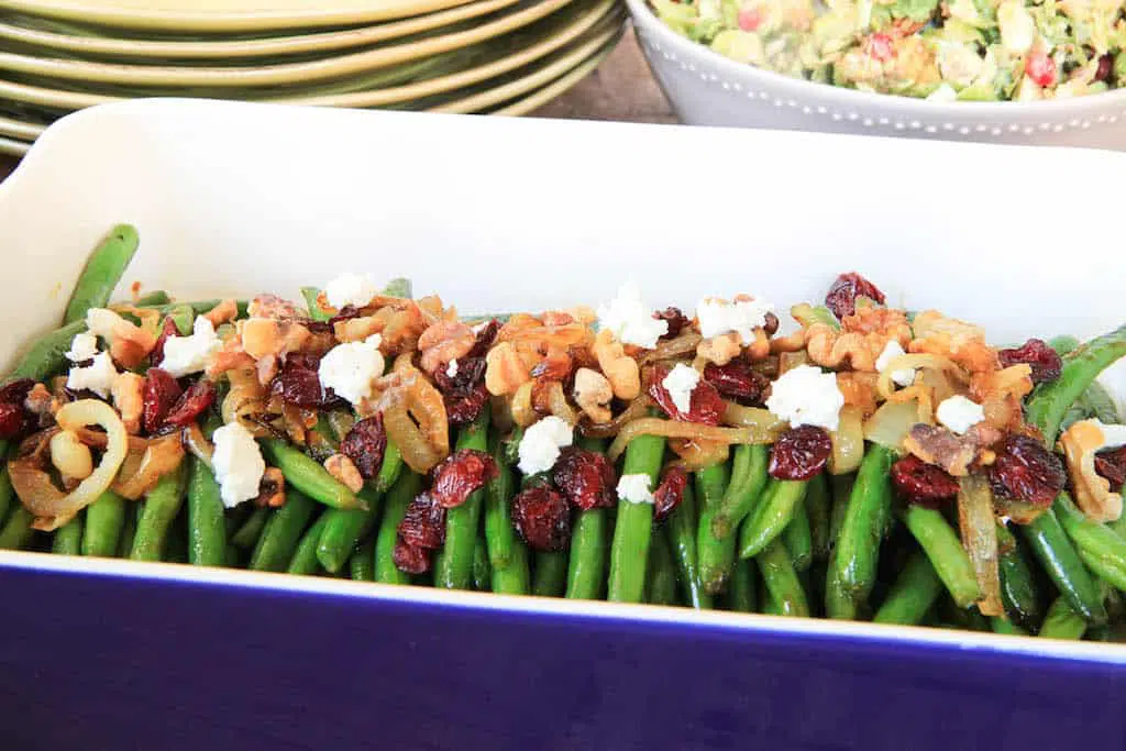 Brown Sugar Glazed Green Beans with Caramelized Onions, Cranberries, Walnuts and Goat Cheese with Plates in the Background