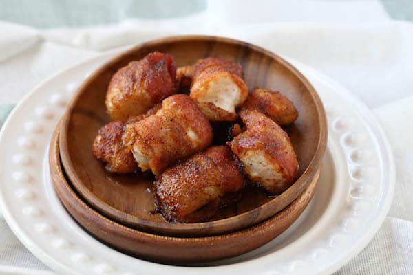 Sweet and Spicy Bacon Wrapped Chicken Bites Ready and Served on a Wooden Disc inside the White Plate on the White Cloth