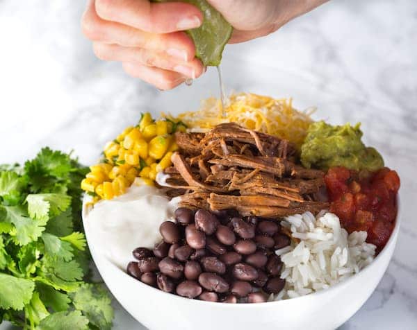 Slow Cooker Barbacoa Beef Burrito Bowls - Squeezing Lime Juice on Top with Parsley at the Side of the White Bowl