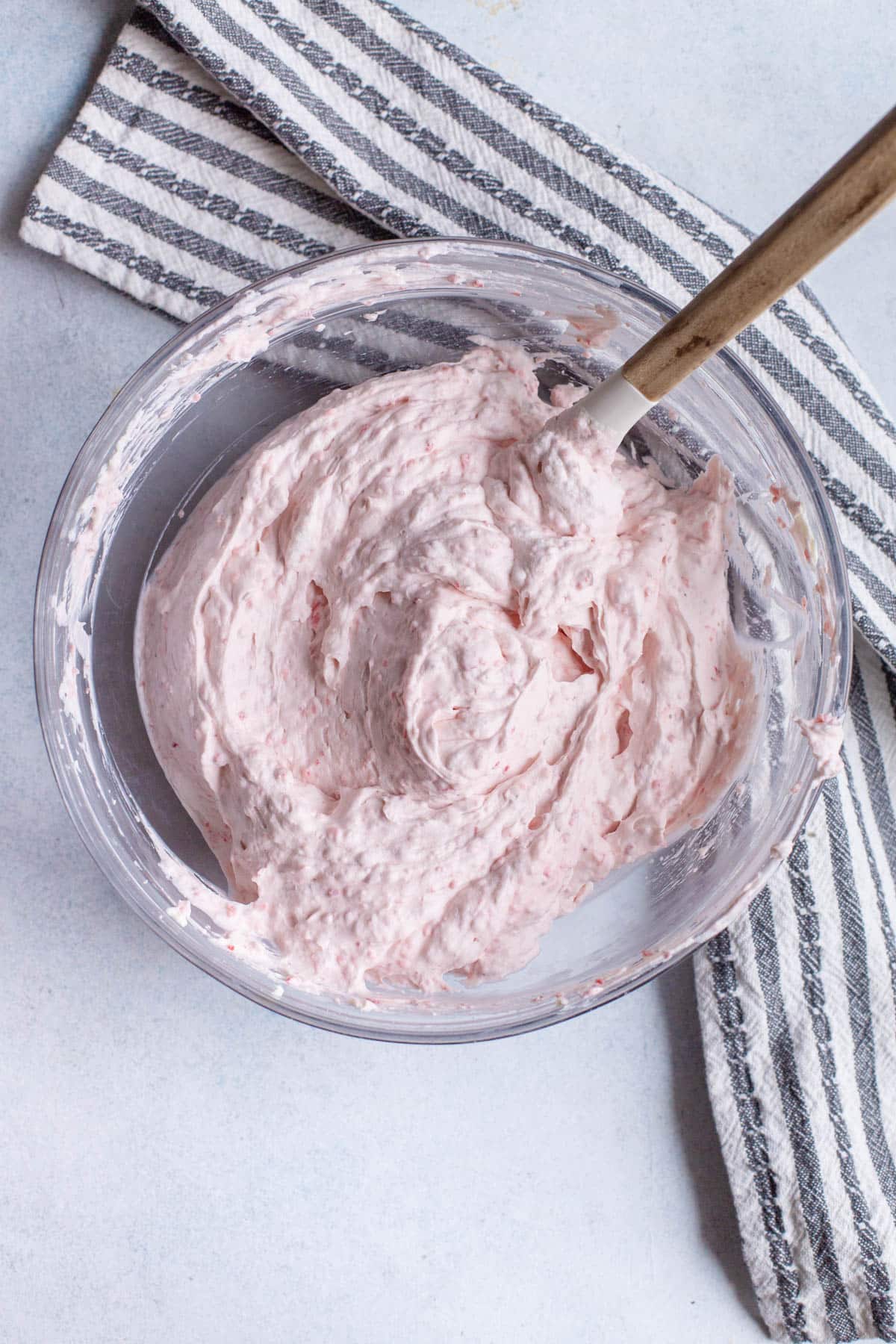 Strawberry cheesecake filling in a glass bowl with a spatula in it.