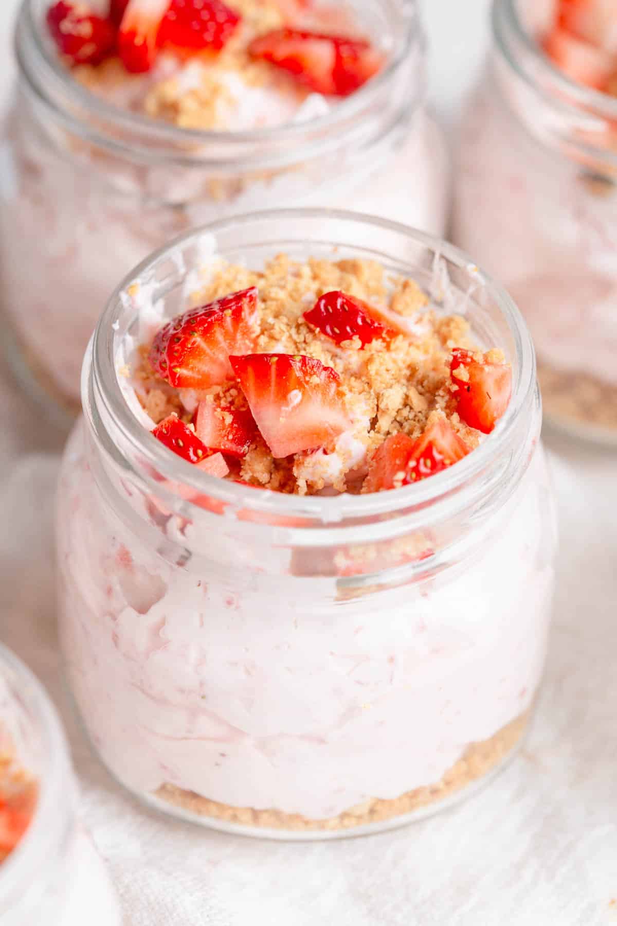 Strawberry Cheesecake Cups in mini mason jars with crumbled graham crackers and diced strawberries on top.