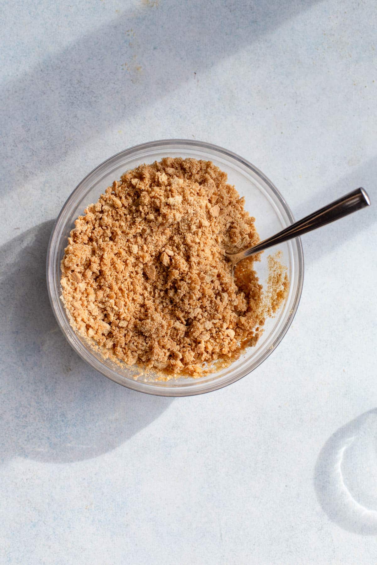 Graham cracker crumbs in a glass bowl mixed with melted butter and sugar.