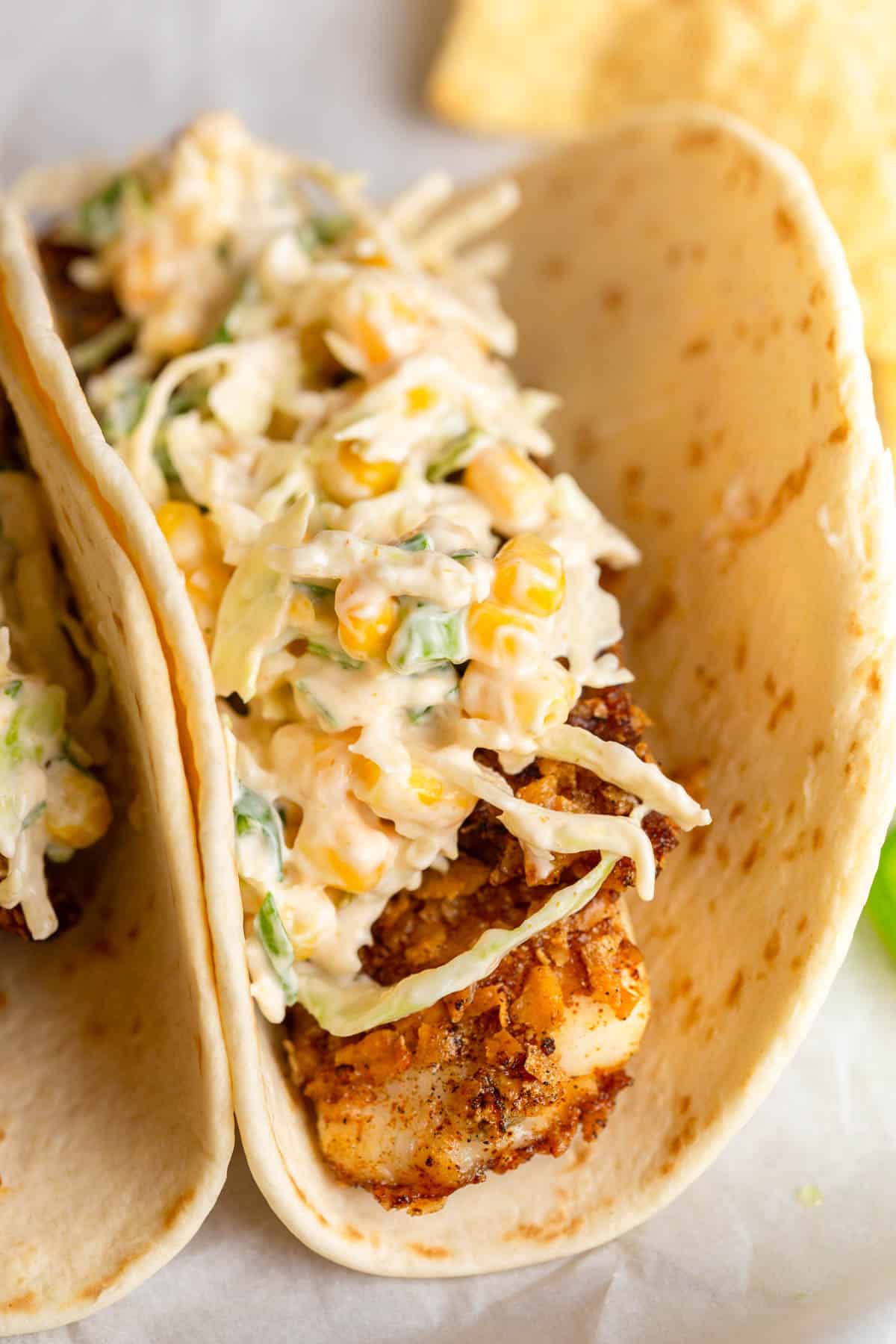 Tortilla Chip Crusted Fish Tacos on a piece of parchment paper with jalapeños and tortilla chips in the background.
