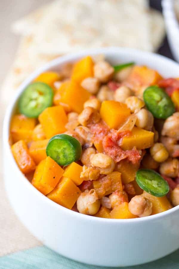 Butternut Squash Chana Masala in a Bowl on the Table with the Rest of the Meal Blurred in the Background