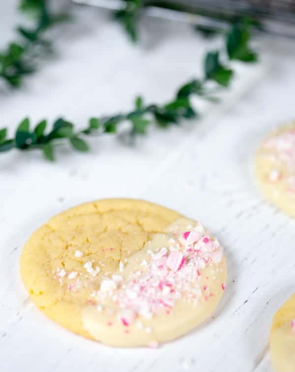 Focus on one of the White Chocolate Dipped Peppermint Sugar Cookies on the table with the greens blurred in the background