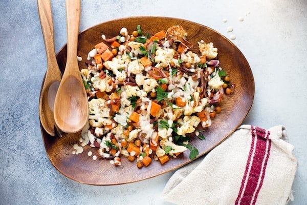 Roasted Cauliflower Sweet Potato Chickpea Salad with Lemon Tahini Dressing - Served in a Wooden Plate with Two Wooden Spoons on the Side and a Cloth Underneath