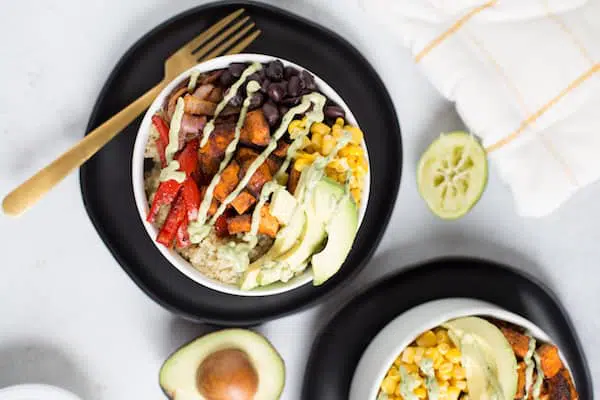 Vegetarian Quinoa Burrito Bowls with Avocado Cream Sauce Overhead on the Served Dish with a Fork, Avocado and Lemon Around the Bowls