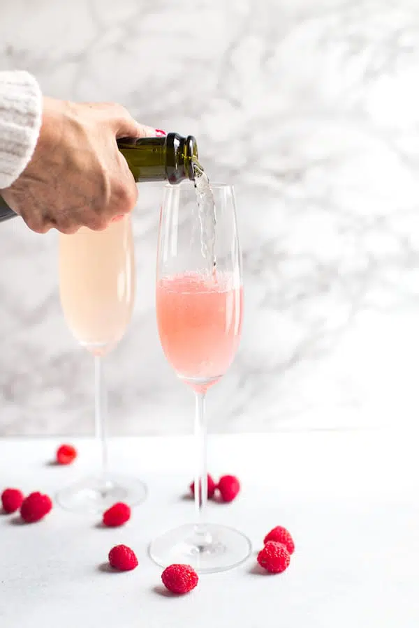 Raspberry Mimosas - Pouring a Bit More of the Drink into the Two Glasses