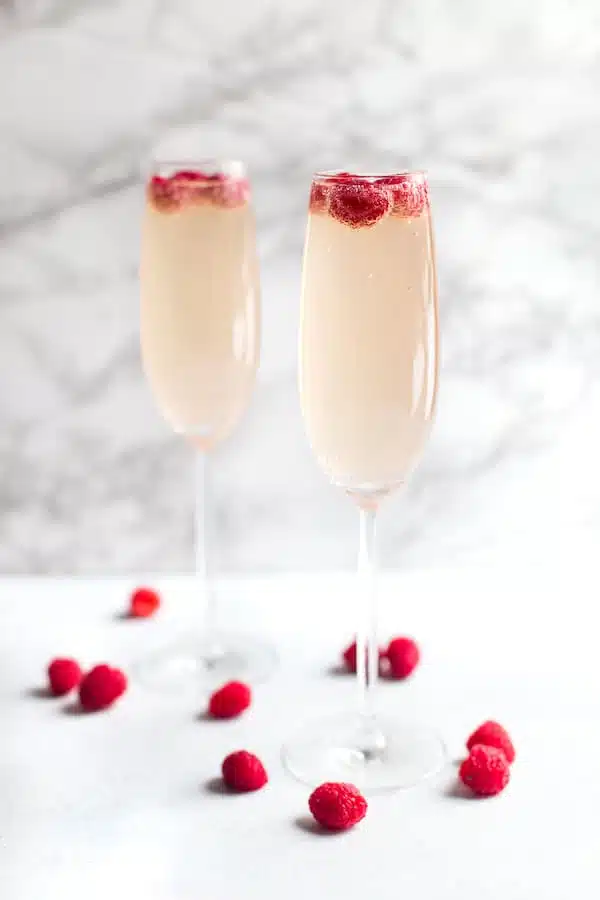 Raspberry Mimosas - Side Shot of Two Glasses with Raspberries Inside and Around on the Table