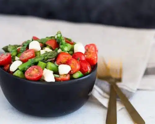 Asparagus Caprese Salad with Two Forks on the Right Side of the Bowl on the Table
