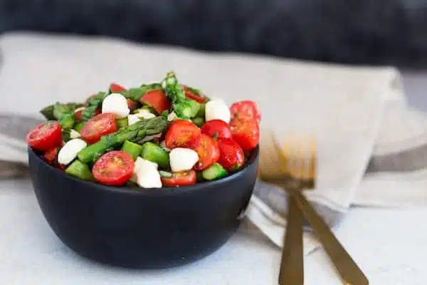Asparagus Caprese Salad with Two Forks on the Right Side of the Bowl on the Table