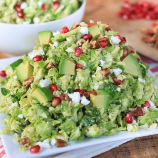 Shredded Brussels Sprout Pomegranate Salad with Honey Mustard Dressing - Served on a White Plate on the Table