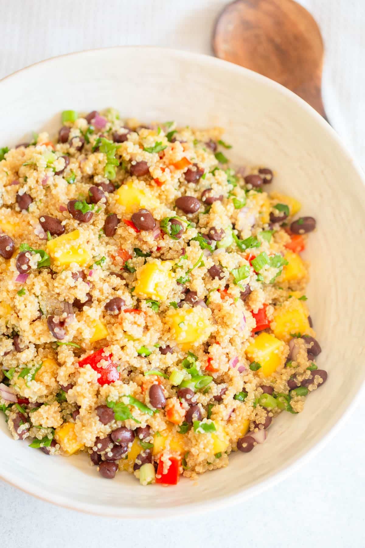 Mango Black Bean Quinoa Salad in a cream colored bowl with a wooden spoon next to it.