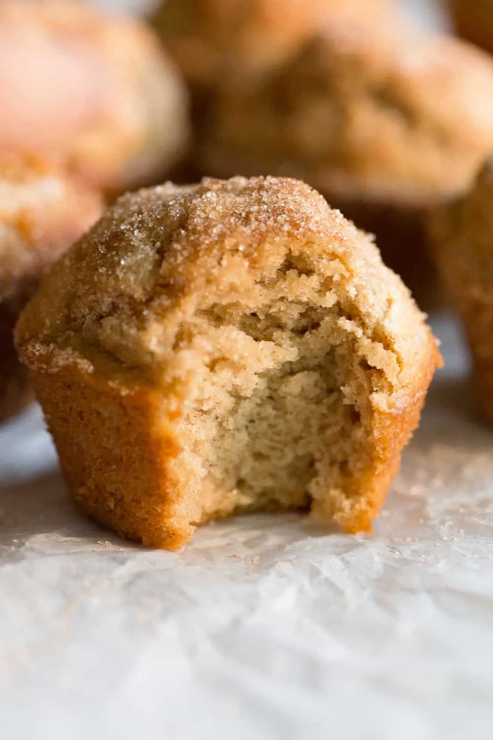 A Maple Donut Muffin on parchment paper with a bite taken out of it 