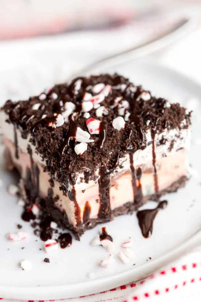 A slice of Peppermint Oreo Ice Cream Cake on a white plate drizzled with hot fudge. 