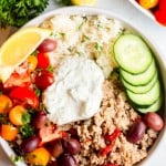 Greek Turkey Rice Bowls in a shallow white bowl with tzatziki on top, tomato salad and fresh parsley in the background.