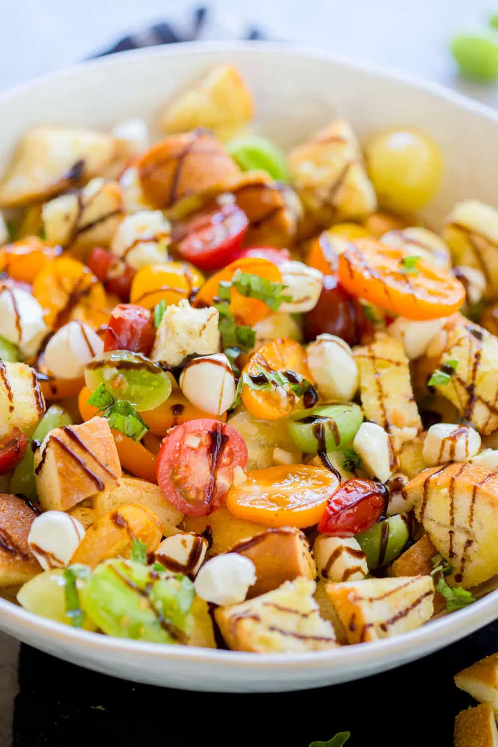 Caprese Panzanella Salad in a shallow cream colored bowl with balsamic glaze drizzled over it.