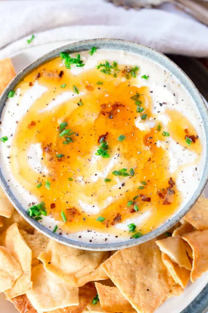 Whipped Feta Dip in a gray bowl surrounded by pita chips, topped with chives and hot honey. 