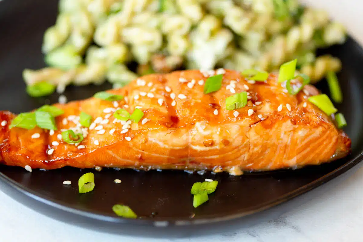 Grilled Teriyaki Salmon on a plate topped with green onions and white sesame seeds. 