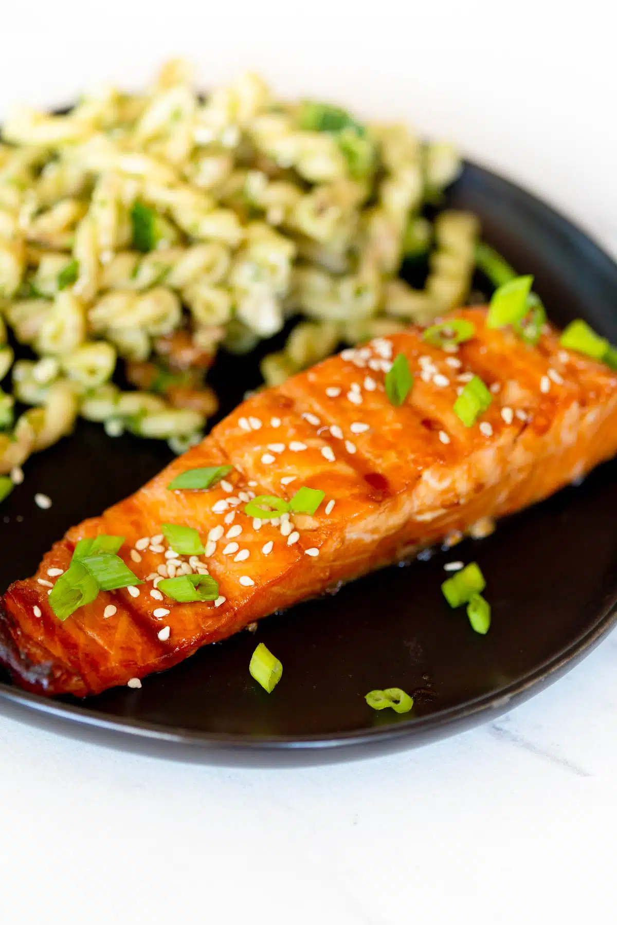 Grilled Teriyaki Salmon garnished with green onions and sesame seeds on a plate with Green Goddess Pasta Salad.