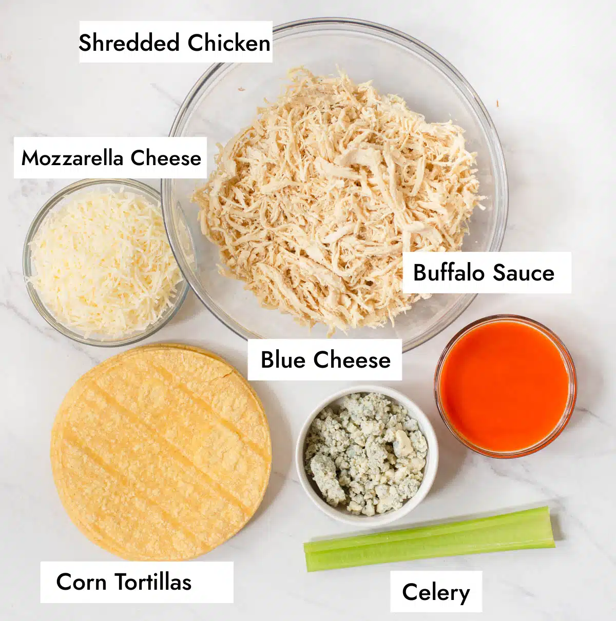 Ingredients in Buffalo Chicken Tacos including shredded chicken, shredded mozzarella cheese, buffalo sauce, celery, blue cheese, and corn tortillas. 