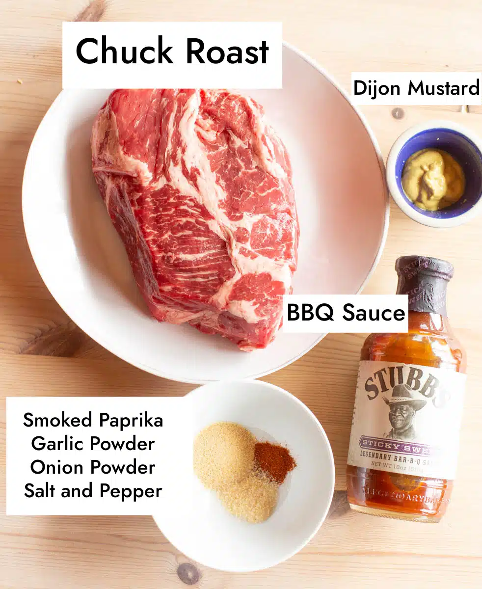 Ingredients in slow cooker BBQ beef including chuck roast, dijon mustard, BBQ sauce, garlic powder, onion powder, salt, pepper, and smoked paprika. 
