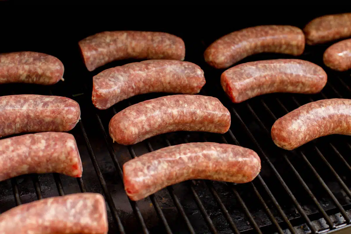 Raw brats placed on the grates of smoker. 