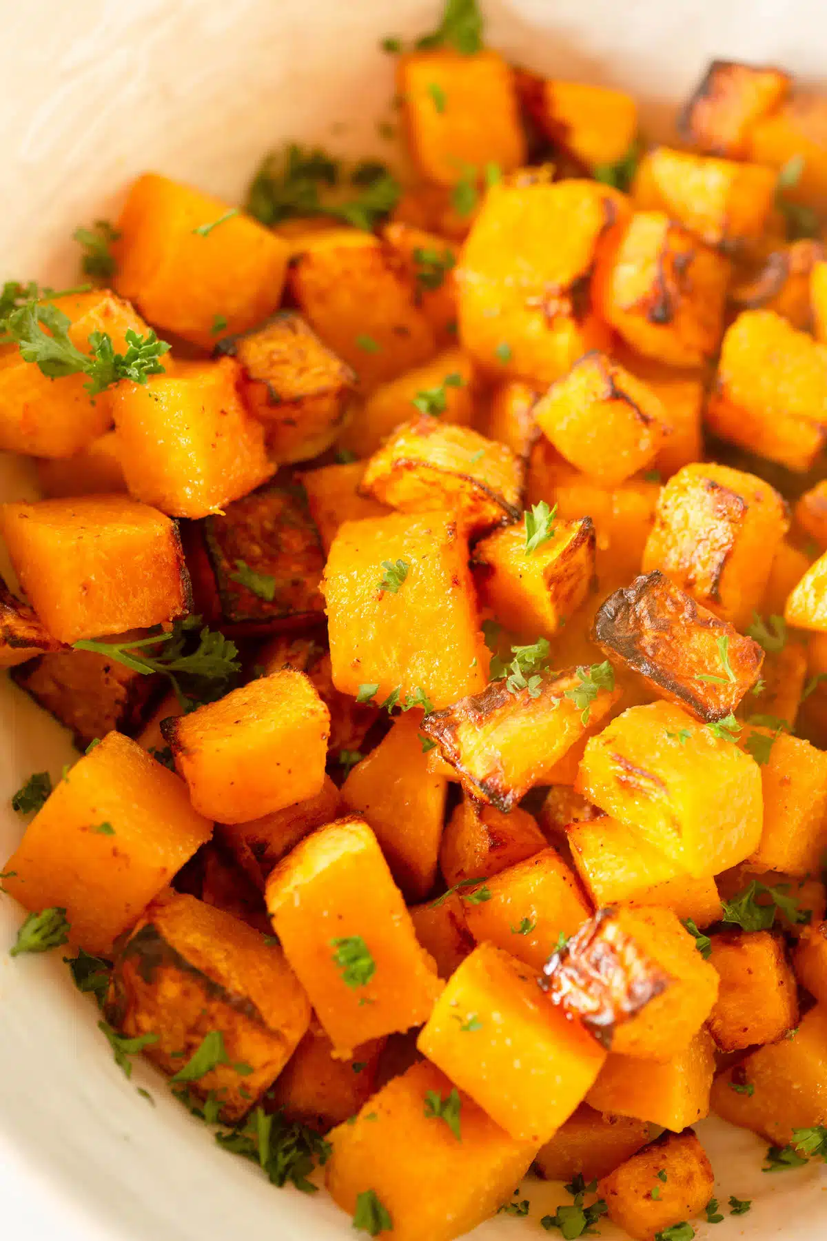Close up of cubed butternut squash sprinkled with chopped parsley. 