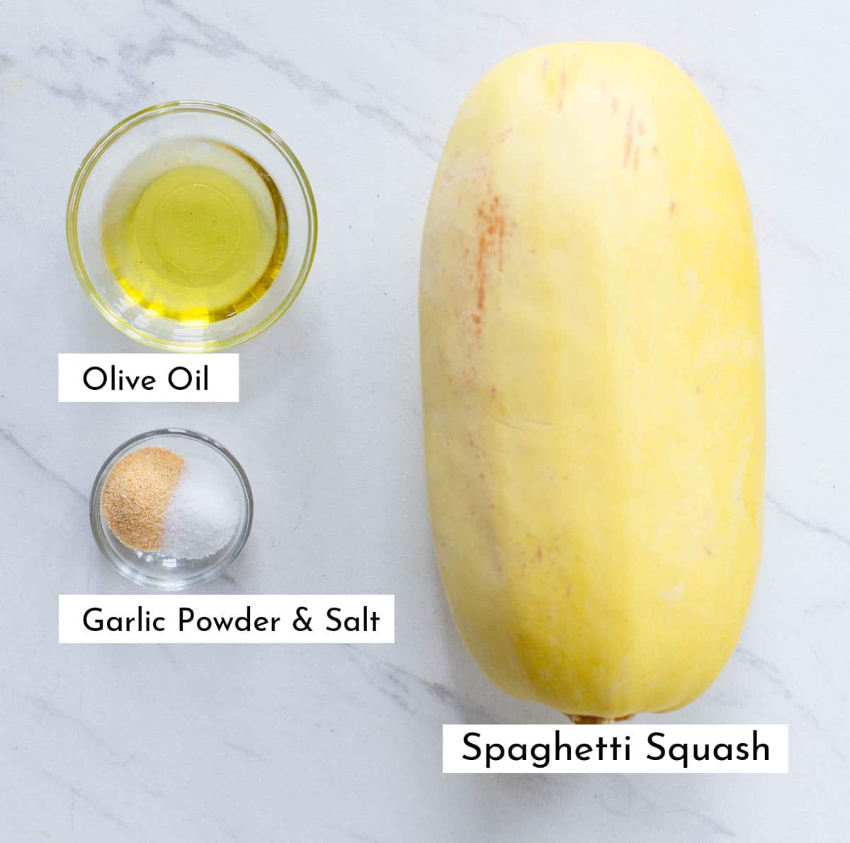 Ingredients in air fryer spaghetti squash, including a whole spaghetti squash, olive oil, garlic powder, and salt on a marbled background.