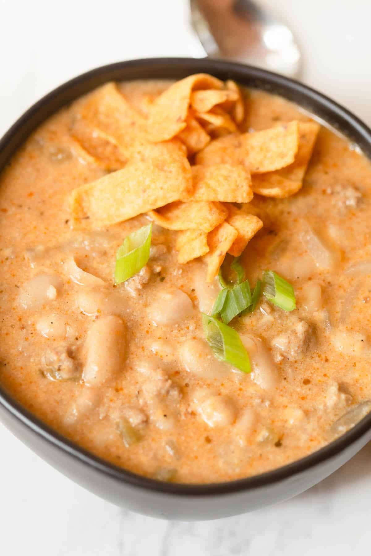 White turkey chili in a black bowl topped with Frito's and diced green onions.