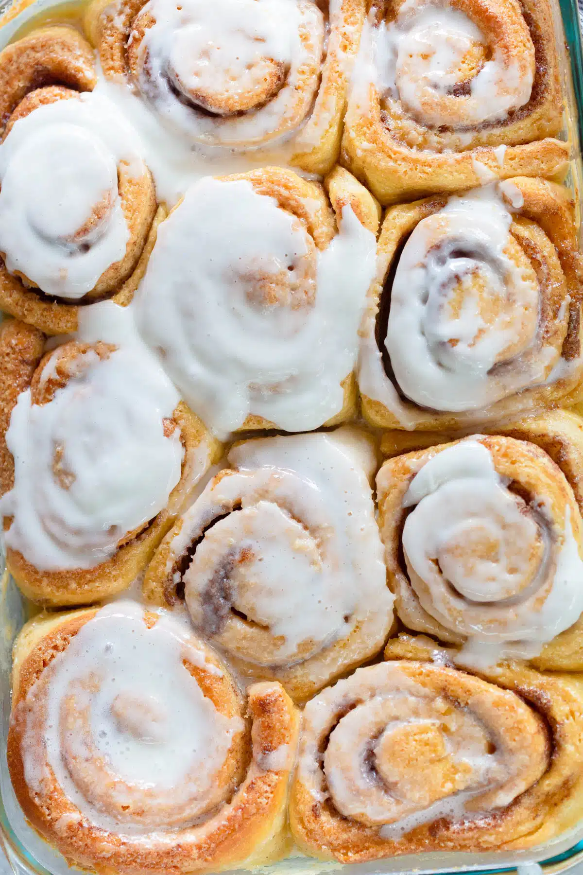 Overhead view of baked golden brown cinnamon rolls in a glass baking dish with frosting. 