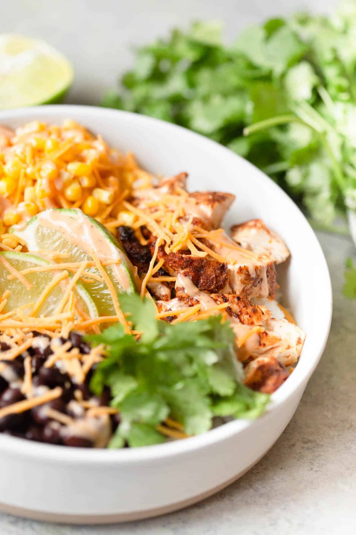 BBQ Chicken Rice Bowls in a white bowl with cilantro and a lime in the background.