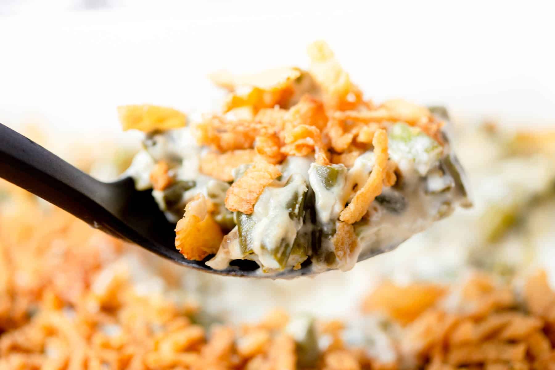 A large scoop of cream cheese green bean casserole in a black serving spoon.