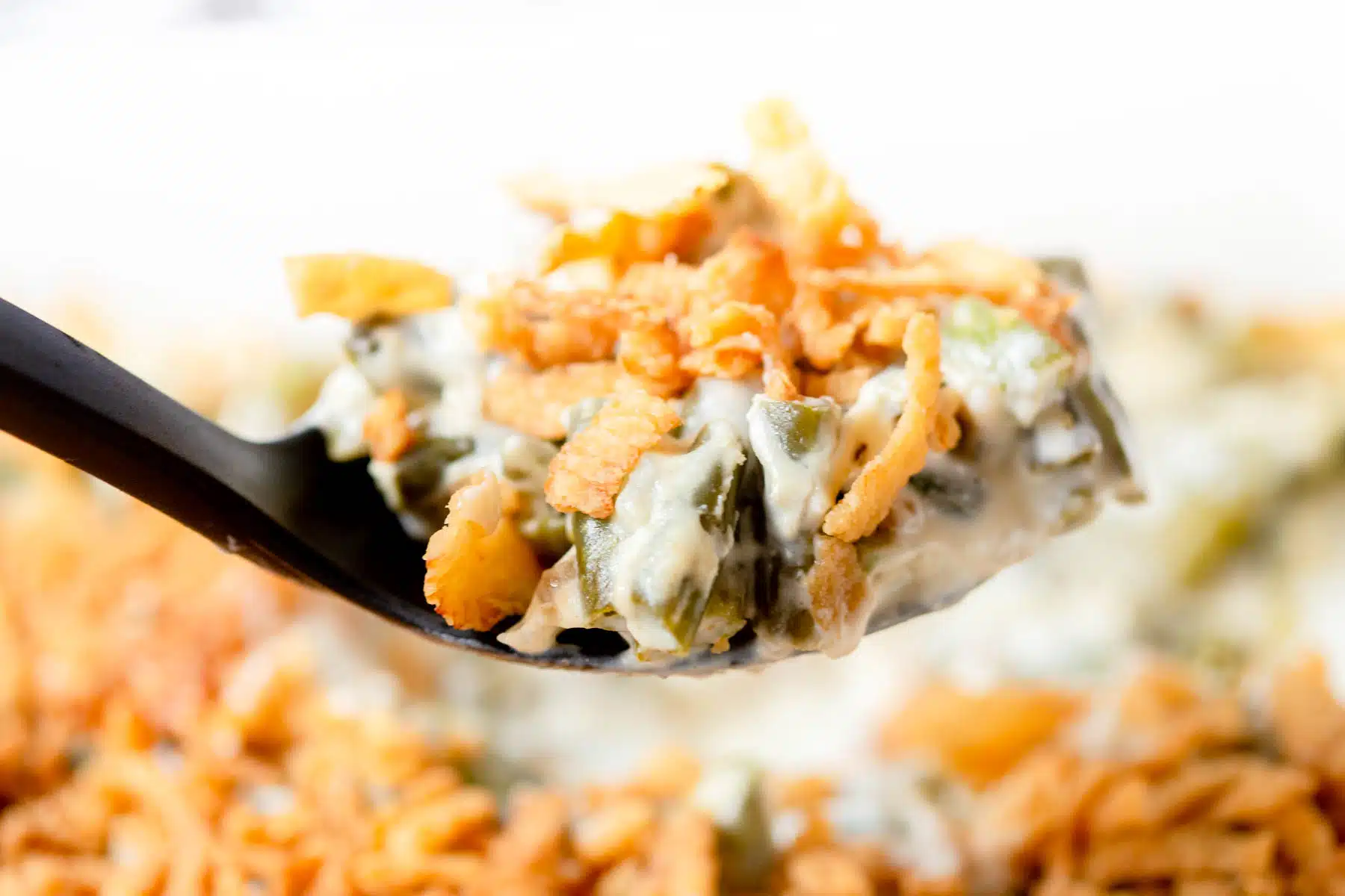 A large scoop of cream cheese green bean casserole in a black serving spoon. 