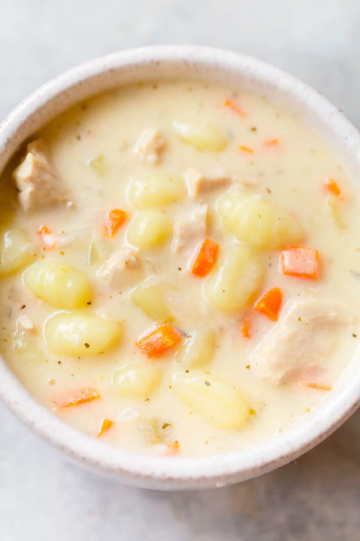 Creamy Turkey Gnocchi Soup in a speckled cream bowl on a gray background. 