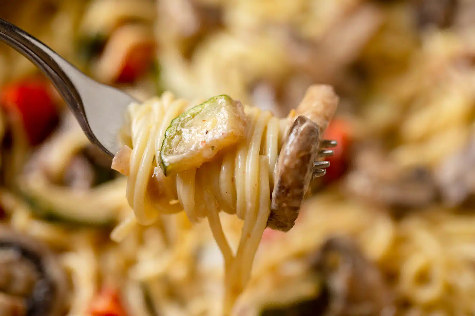 Creamy Vegetable Pasta twirled around a fork with a piece of mushroom on the end of the fork and a piece of zucchini on top of the noodles. 