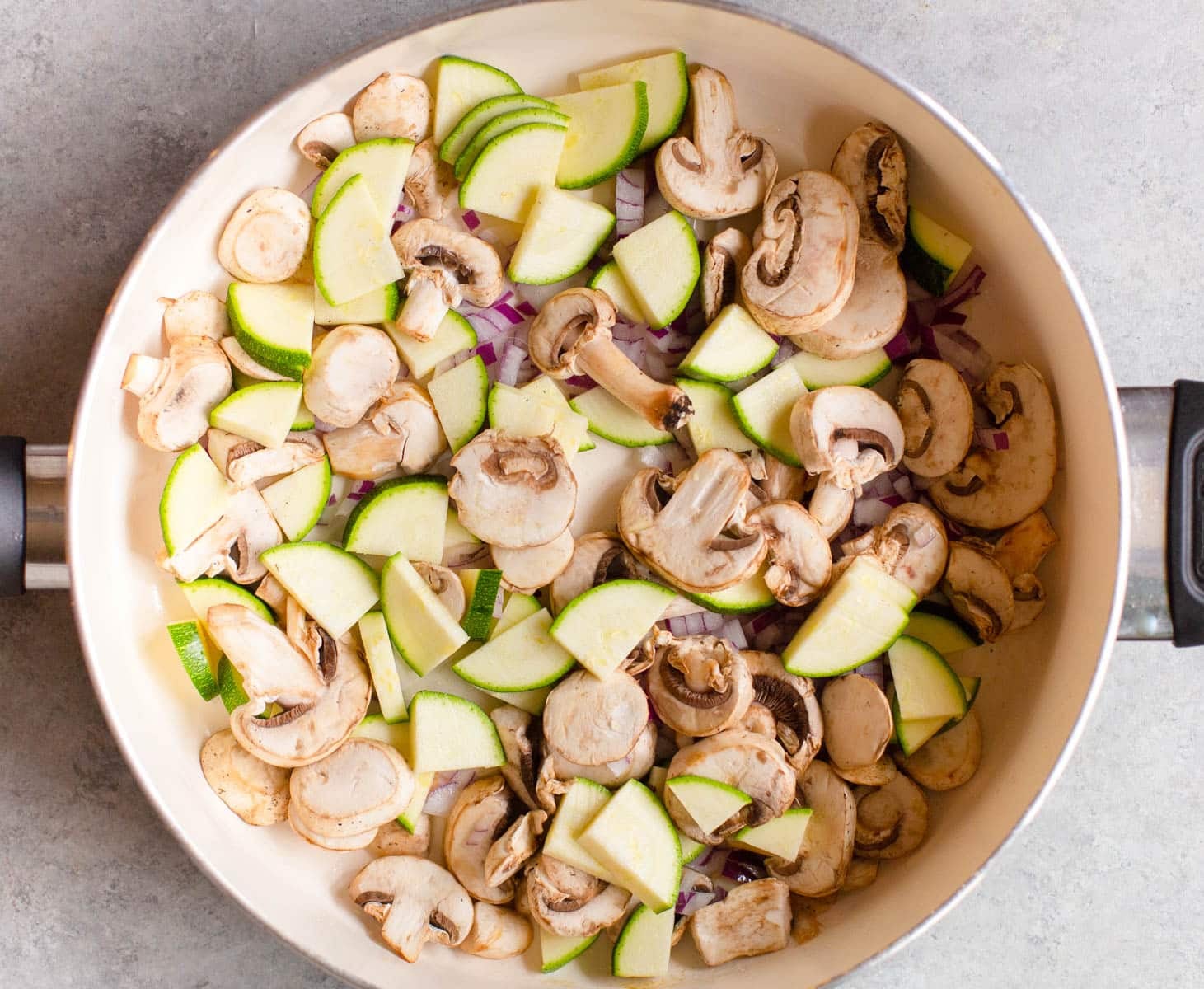 White pan with diced zucchini and mushrooms in it.