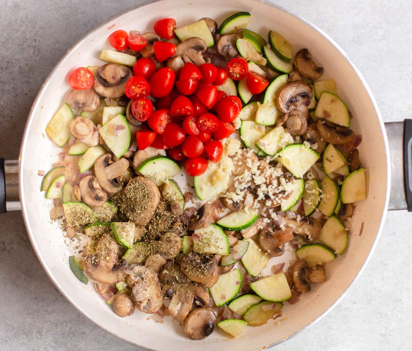 White pan with diced zucchini, tomatoes, garlic, herbs, and mushrooms in it.