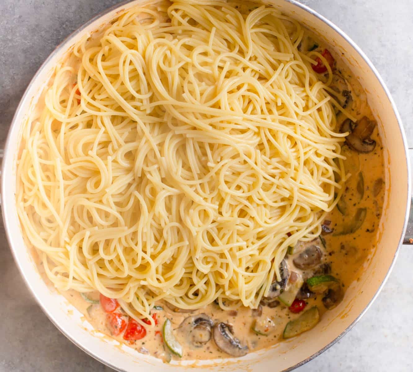 White pan with a creamy vegetable sauce in it and spaghetti noodles on top.