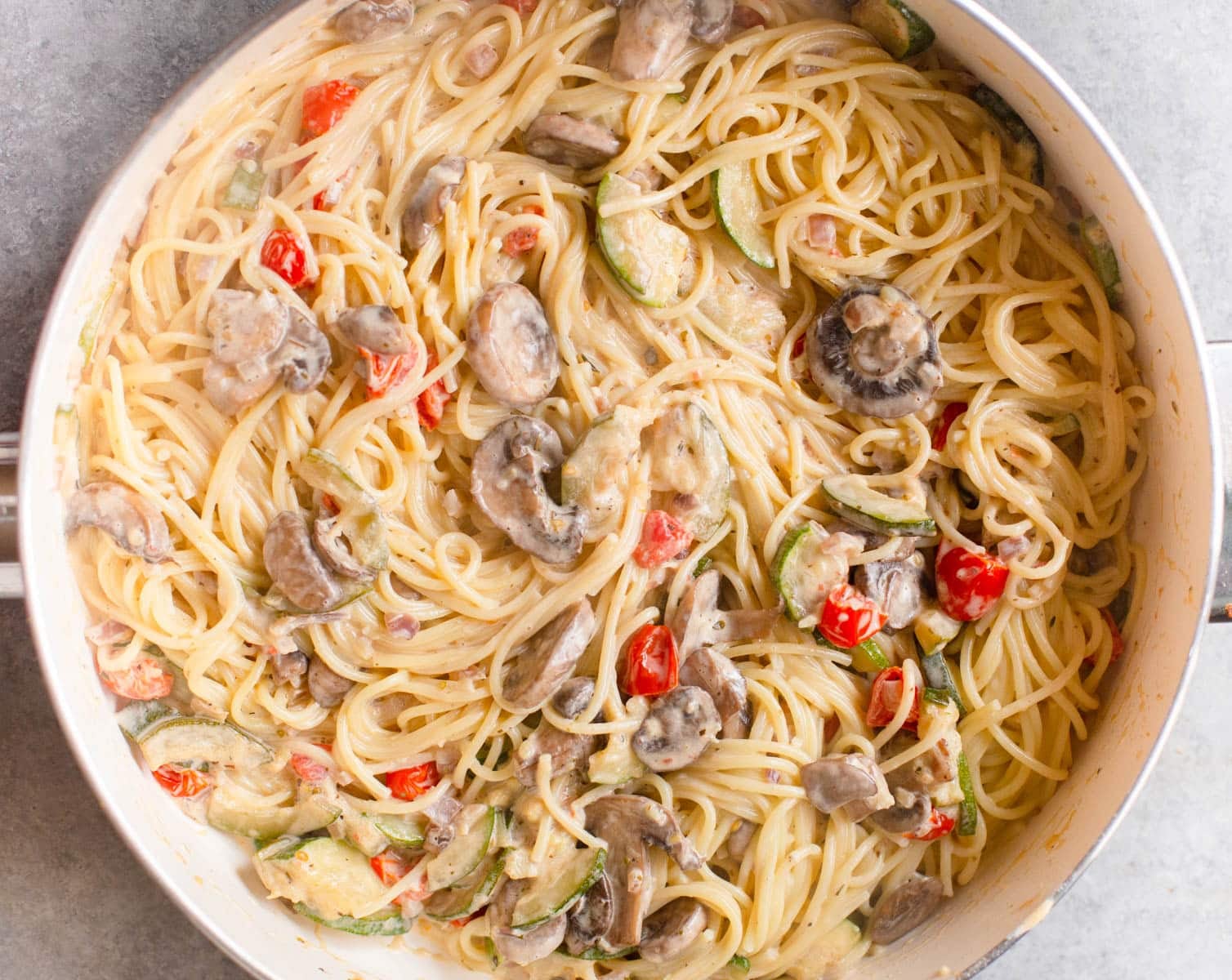 White pan with spaghetti tossed in a creamy vegetable sauce.
