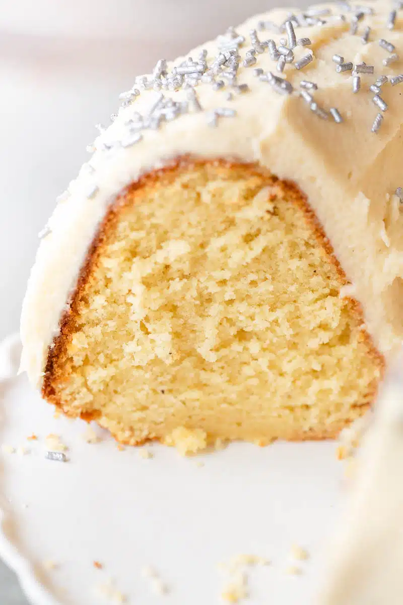 Boozy Eggnog Bundt Cake with frosting and silver sprinkles on a white cake platter. 
