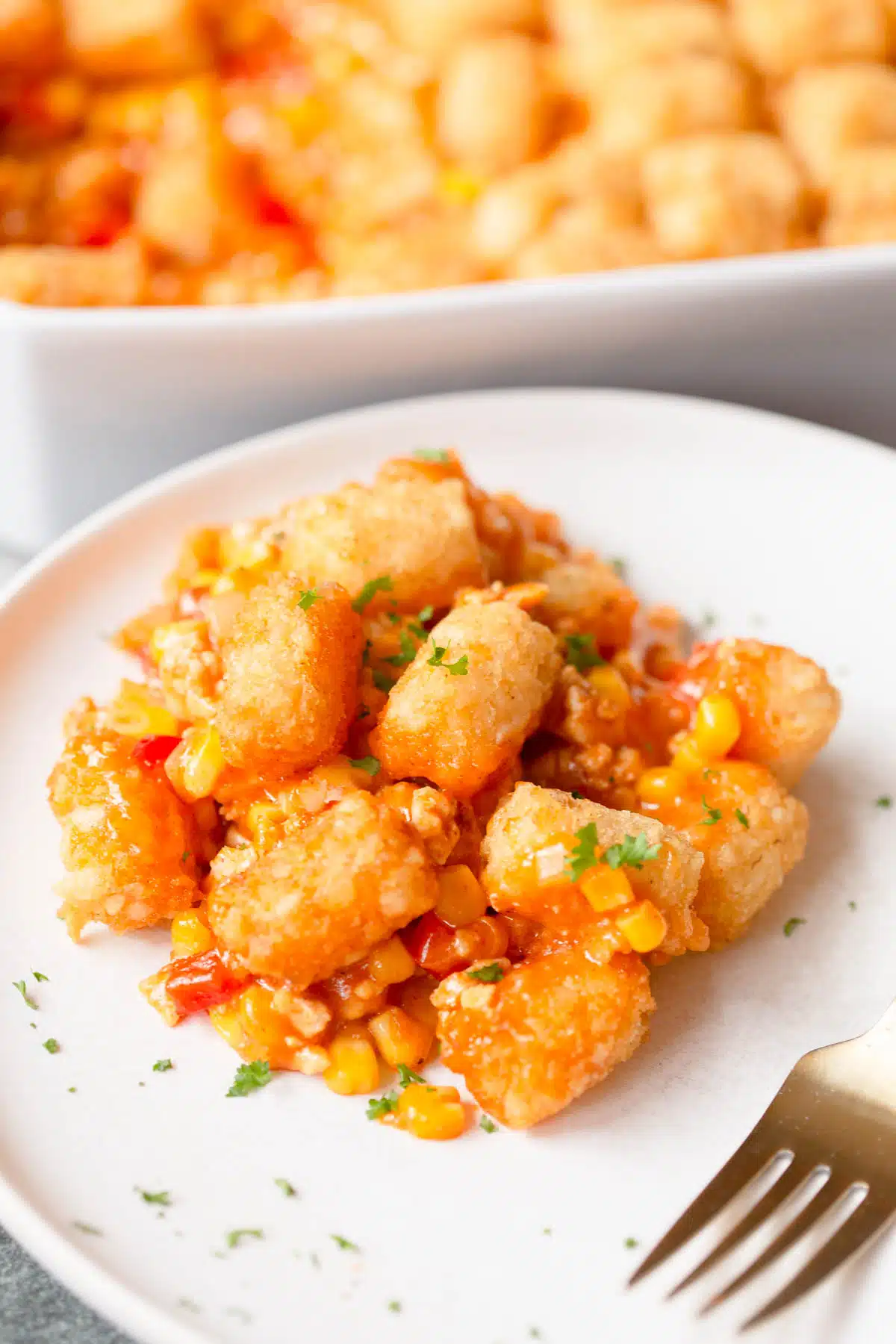 Mexican Tater Tot Casserole on a white plate with a gold fork, with chopped cilantro on top and around the plate.