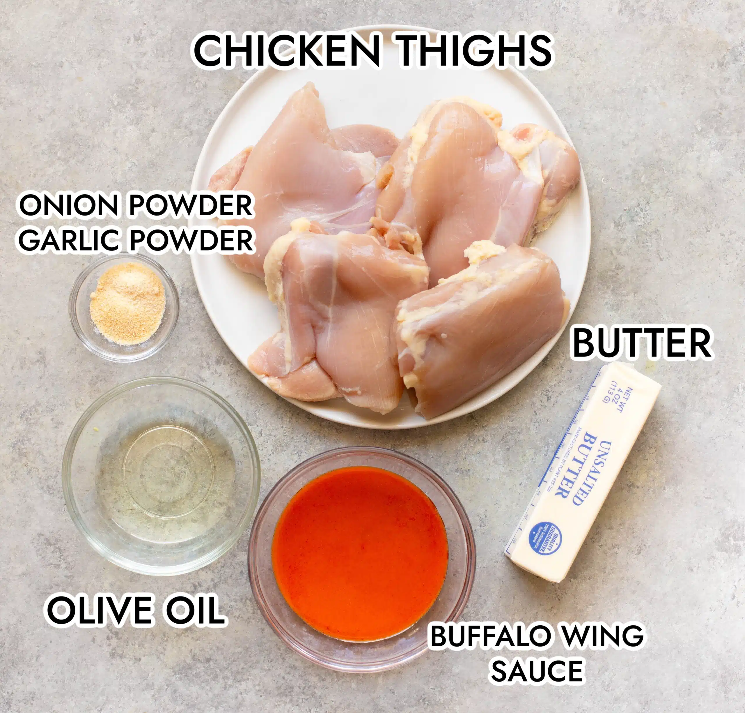 Ingredients for air fryer buffalo chicken thighs on a gray background, including chicken thighs, onion powder, garlic powder, olive oil, buffalo wing sauce, and butter.
