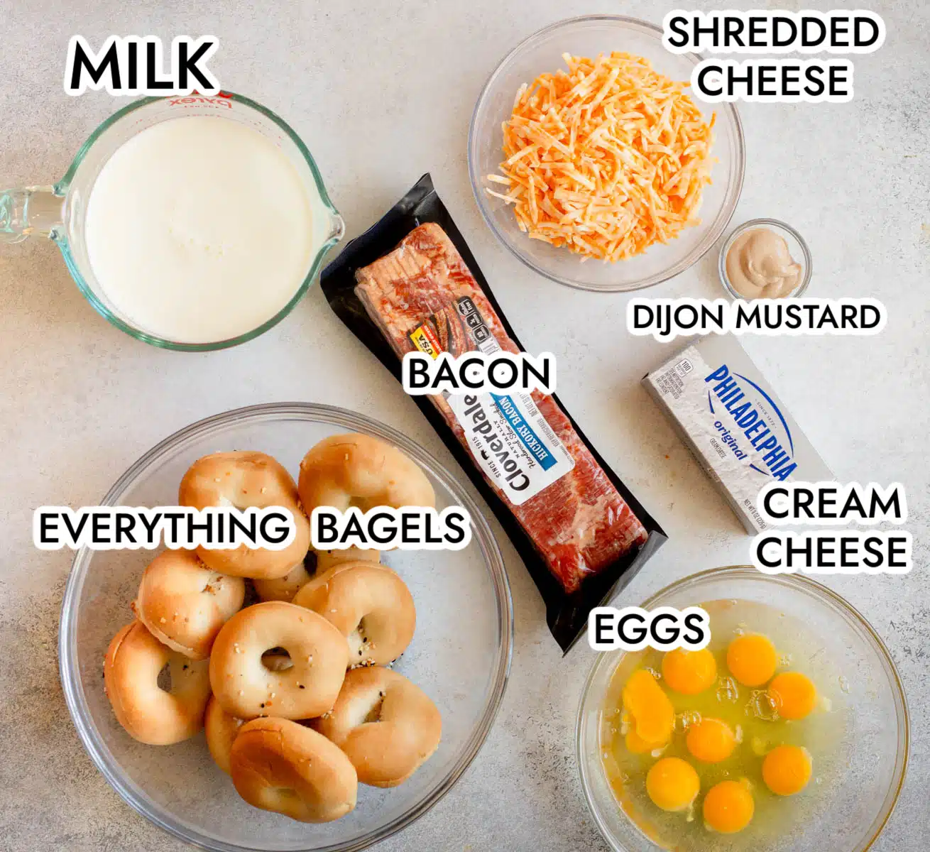 Ingredients in Everything Bagel Casserole including milk, bacon, cheese, dijon mustard, cream cheese, eggs, and bagels. 