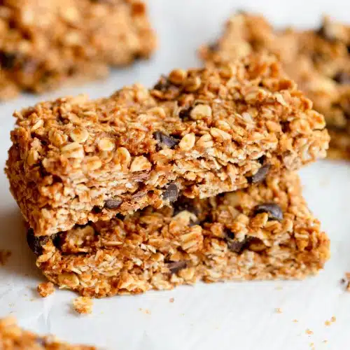 Almond Butter Oat Bars - two stacked on top of each other on parchment paper with other bars in the background.