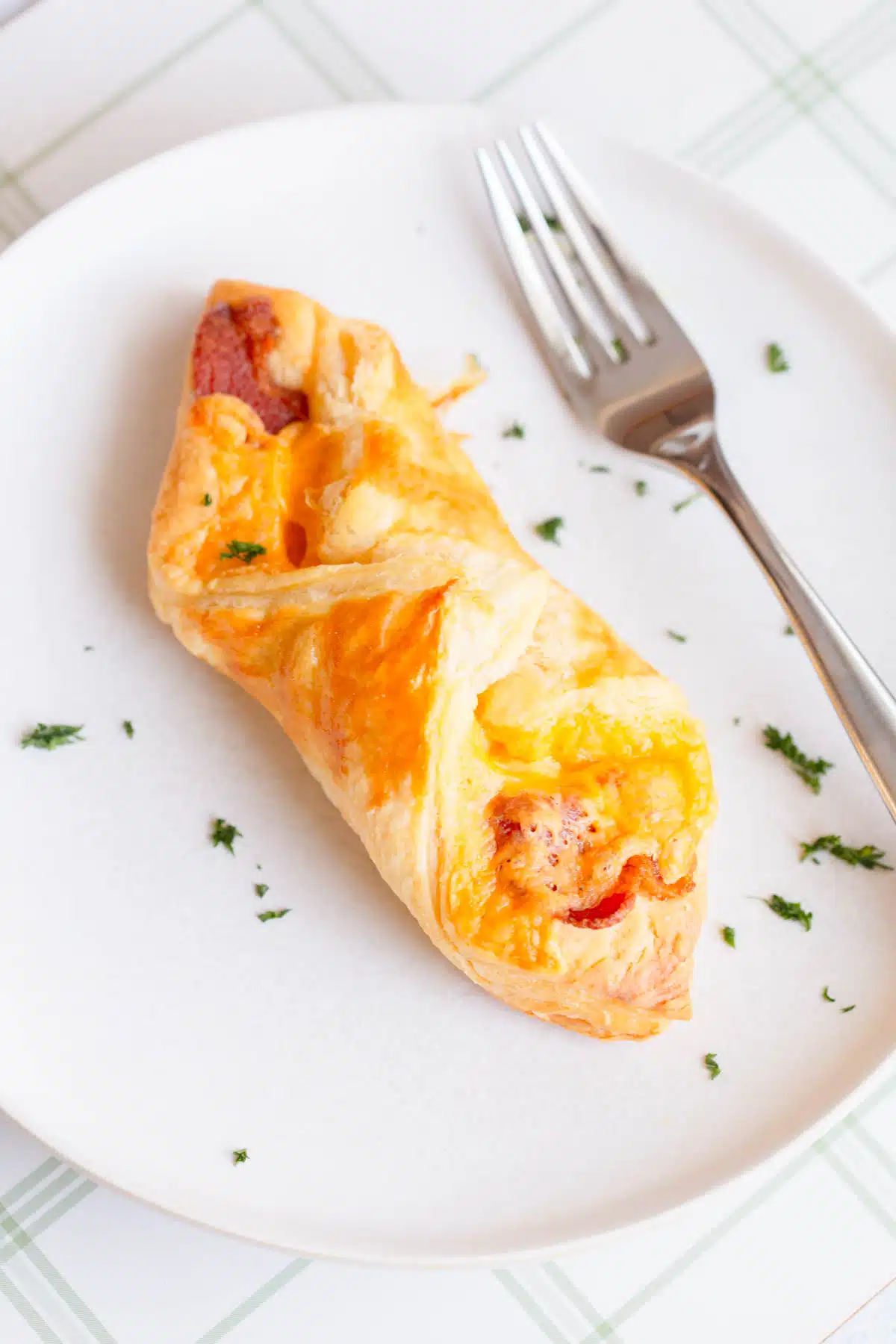 Bacon Cheese Turnover on a white plate with parsley sprinkled on top, and a fork next to it. 
