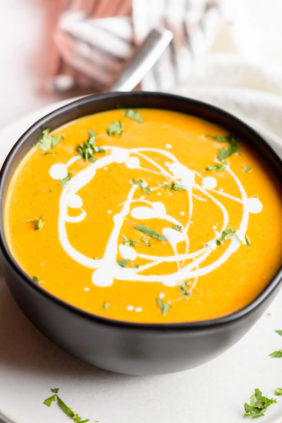 Carrot Pumpkin Soup in a black bowl drizzled with coconut milk and sprinkled with fresh cilantro and green onions. 