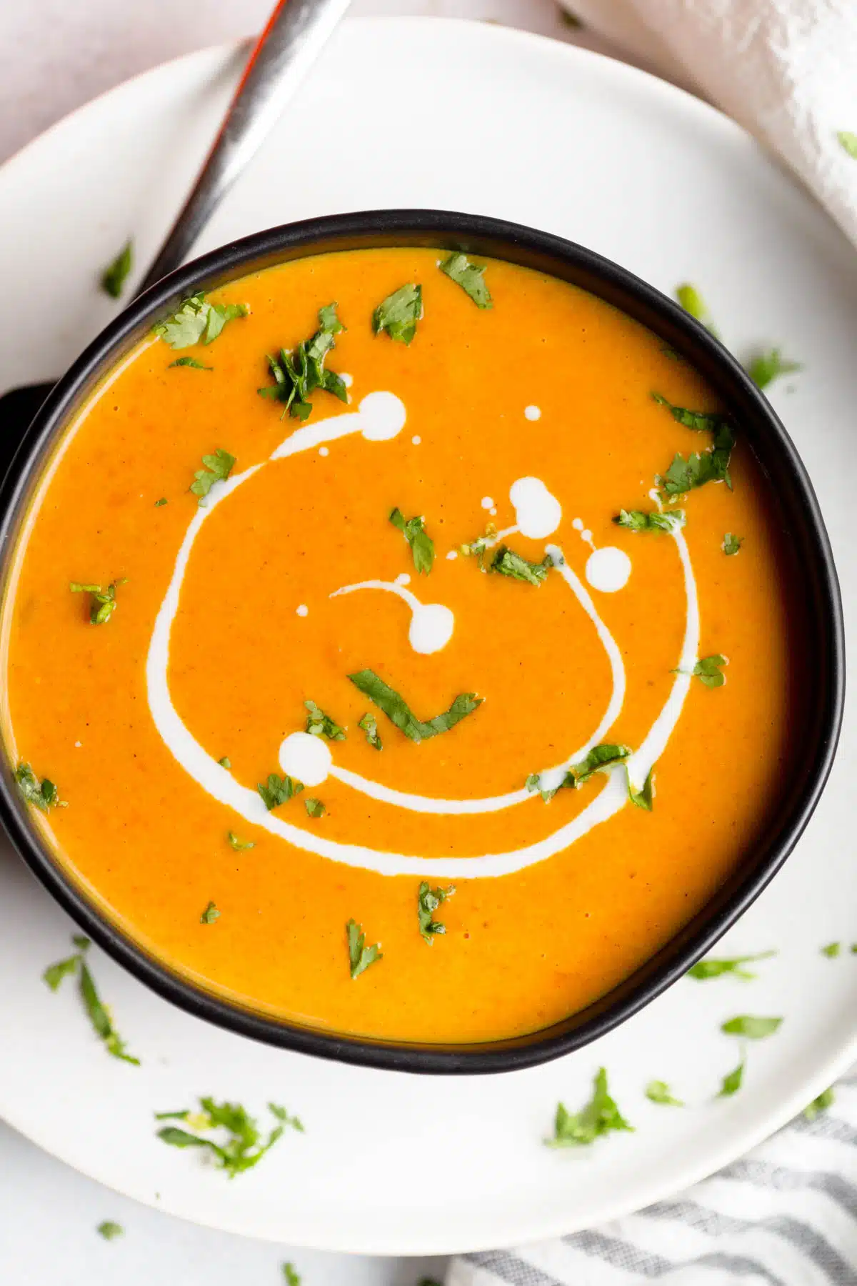 Carrot Pumpkin Soup in a black bowl drizzled with coconut milk and sprinkled with fresh cilantro and green onions. 