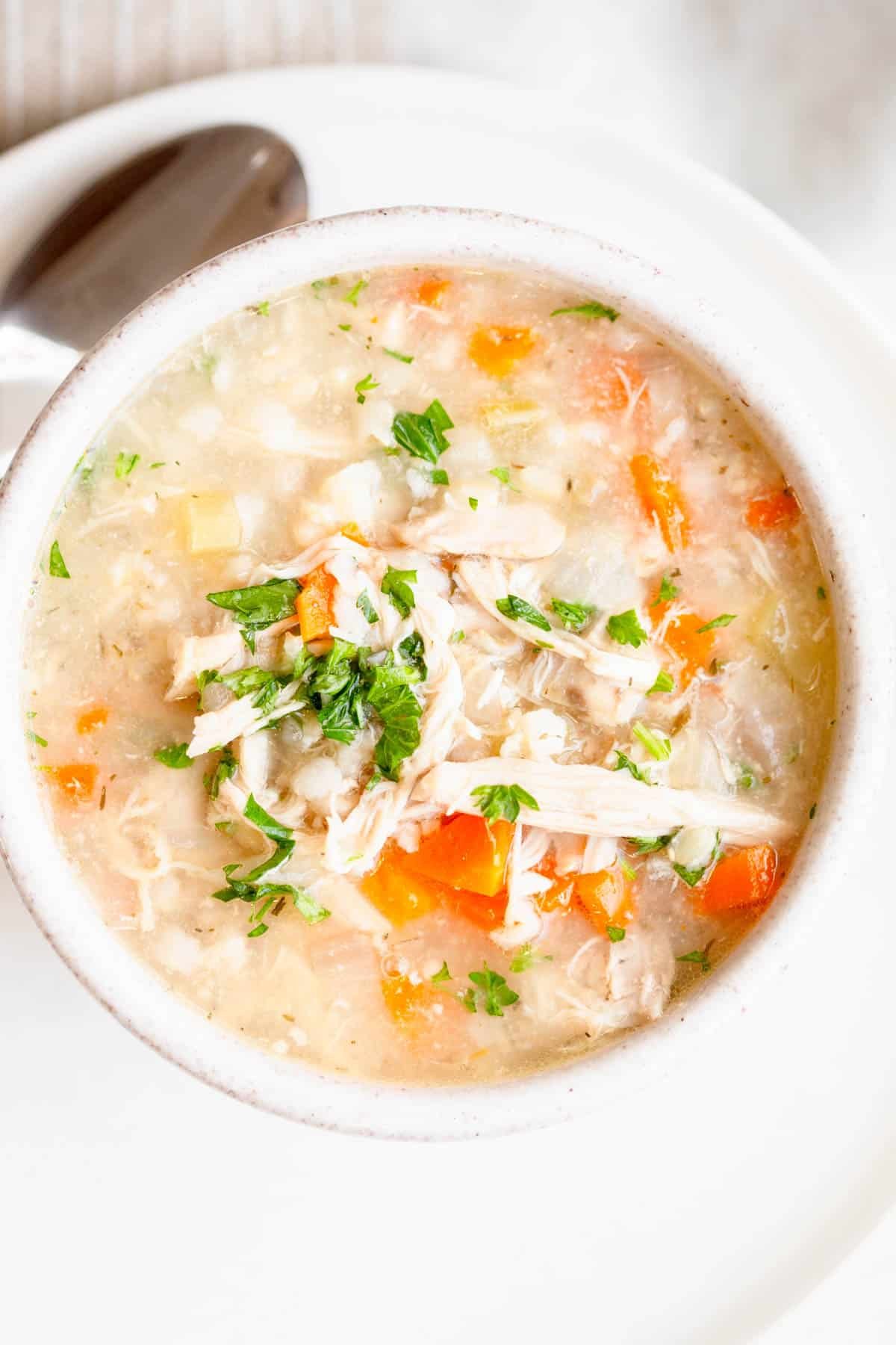 Crock Pot Chicken Rice Soup in a speckled cream bowl with a soup spoon on the plate next to it. 