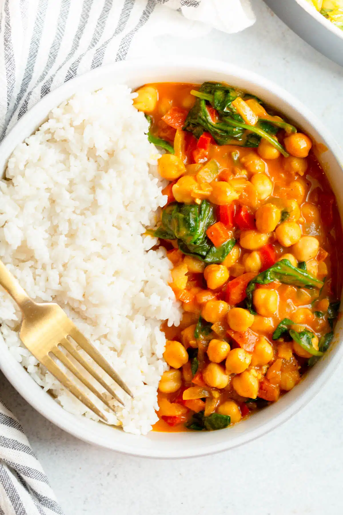 Spinach Chickpea Curry in a bowl with coconut rice and a gold fork on top of the rice. 